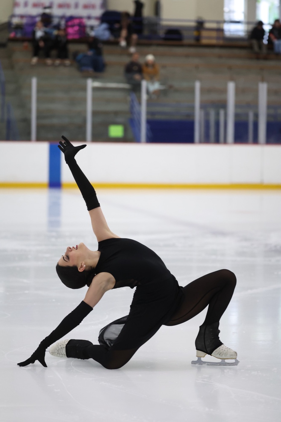 Abril in a black costume and long gloves, arched back in a lunge on the ice